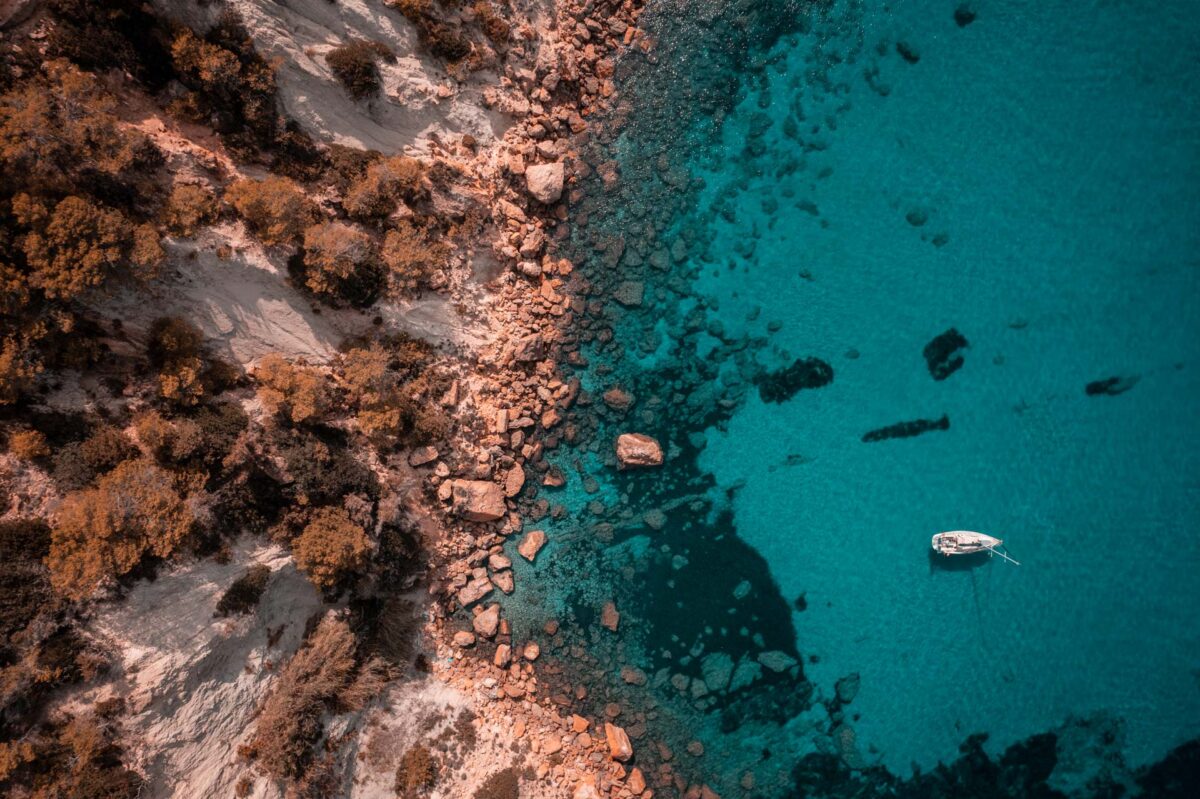 Drone shot of a yacht anchoered in Ibiza, near the shoreline.