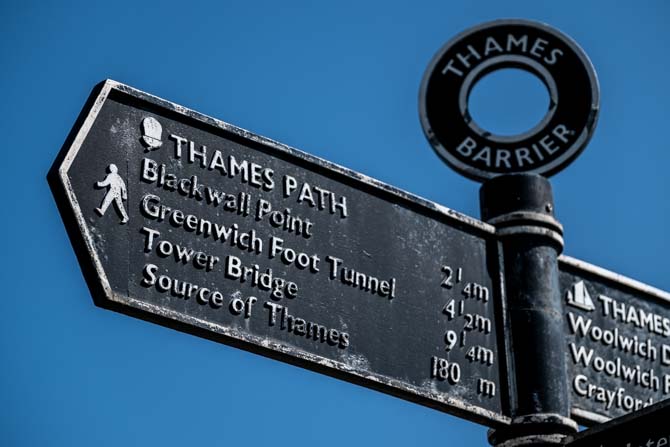 A metal sign with the words Thames Barrier providing directions to Blackwall Point, Geenwich foot Tunnel, Tower Bridge and Source of Thames, along with distances.