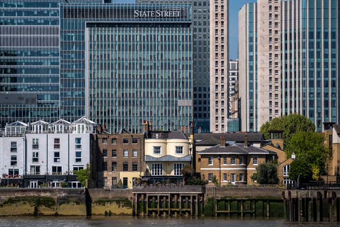 Houses on the side of the River Thames are dwarfed by the skyscrapers of Canary Wharf