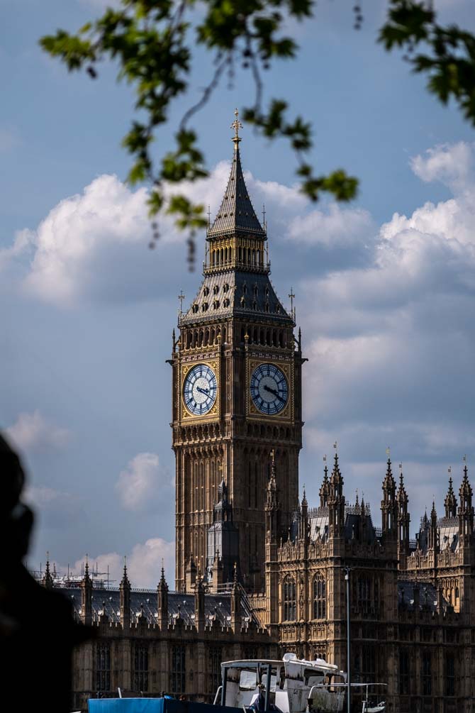 Elizabeth Tower of the Houses of Parliament with boats in the foreground and trees overhanging in the frame of the picture.